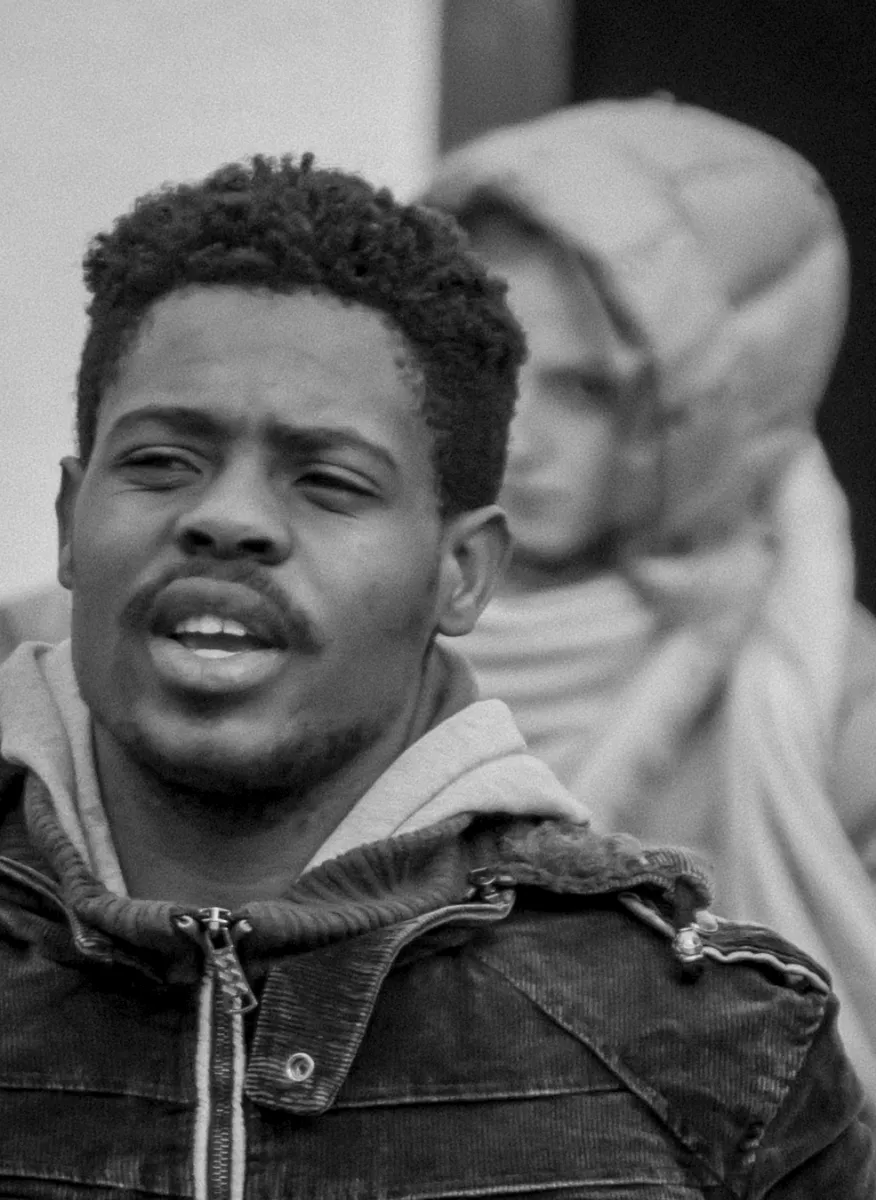 Young man in a denim jacket with a headscarfed statue blurred behind him